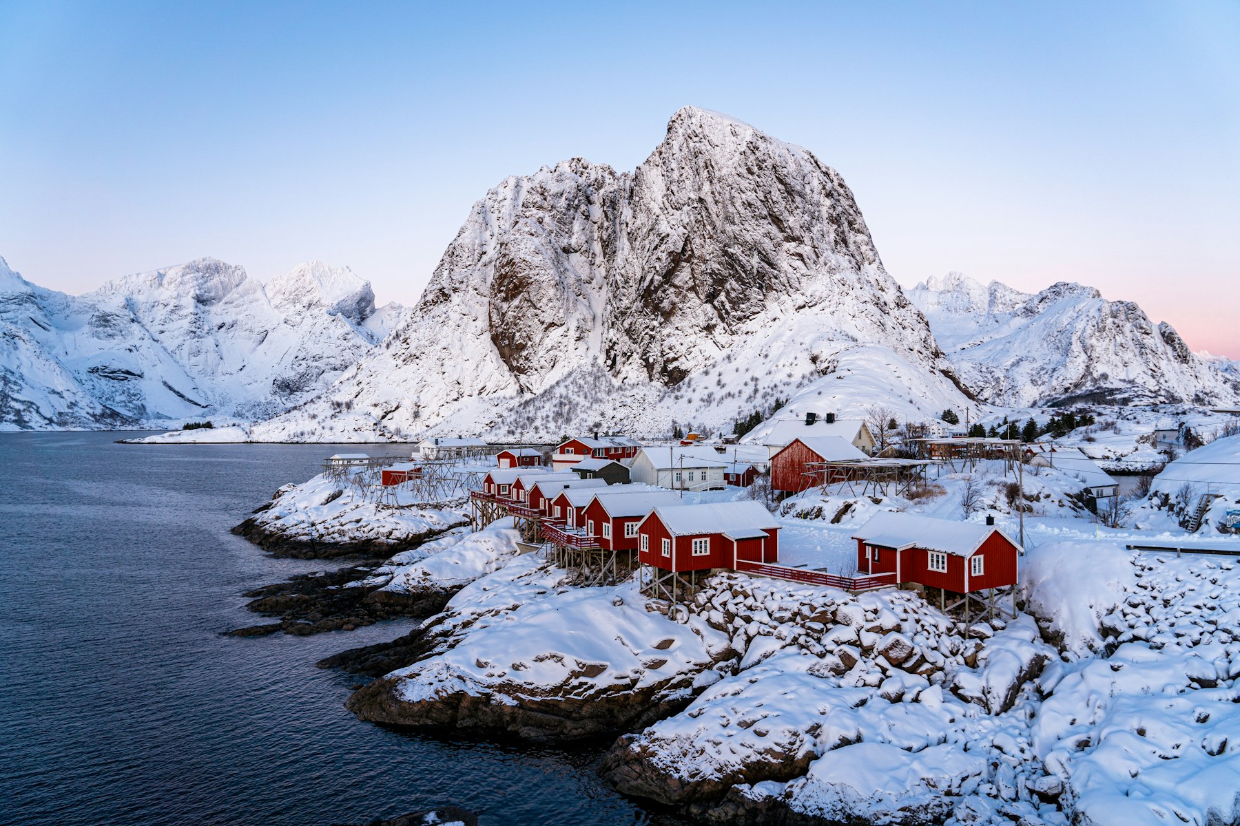 Snow-covered Lofoten mountains above red coastal cabins in Norway